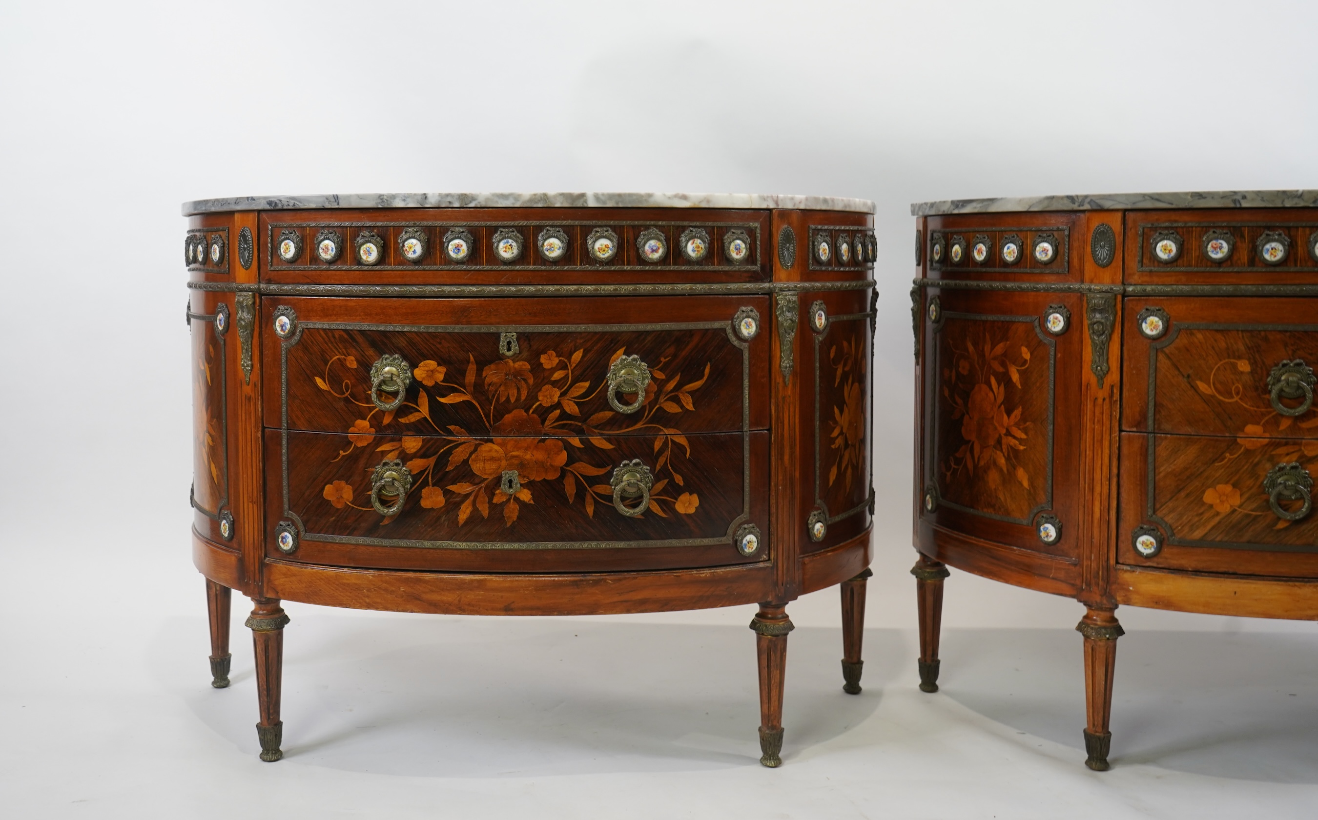 A pair of early 20th century French marquetry inlaid, gilt metal and porcelain mounted rosewood and beech demi-lune commodes